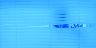 A person peeping through a set of white Venetian blinds